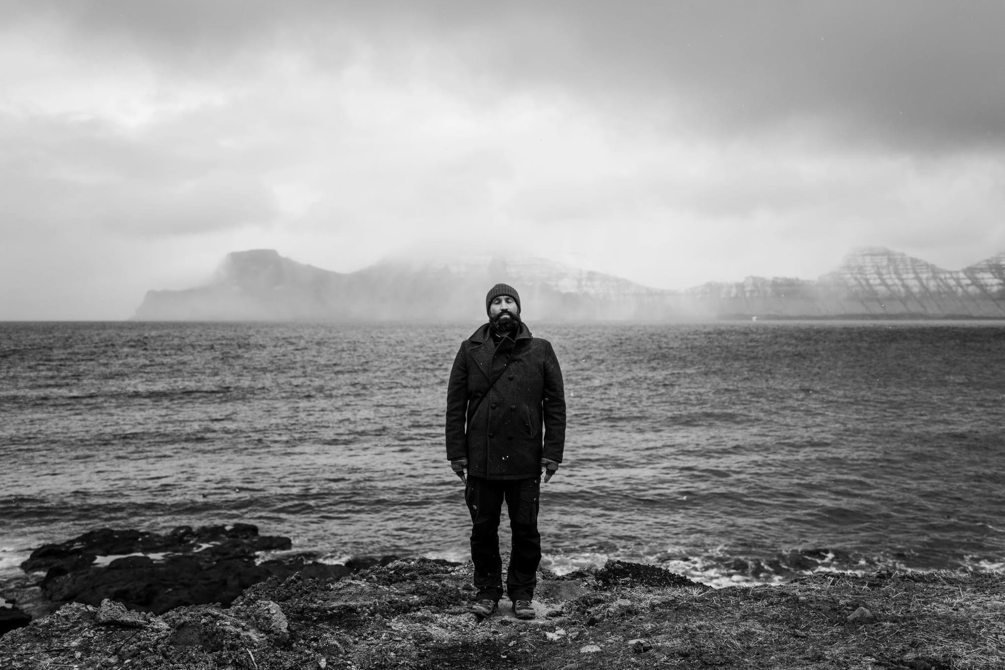 Elopement photographer Chris from Sturmsucht stands by the Faroe Islands' rugged coast, capturing moody, adventurous vibes